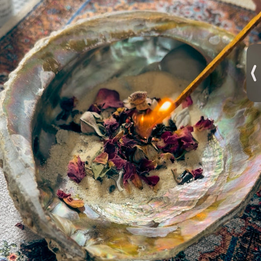 Abalone filled with sand and Moroccan Rose Buds being lit by a  ceremonial match for a burning release ceremony - For the Love of Natural Living, LLC 